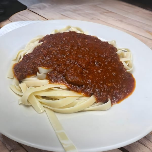 A white plate of Romano's fettuccine pasta topped with a rich, dark red Bolognese sauce.