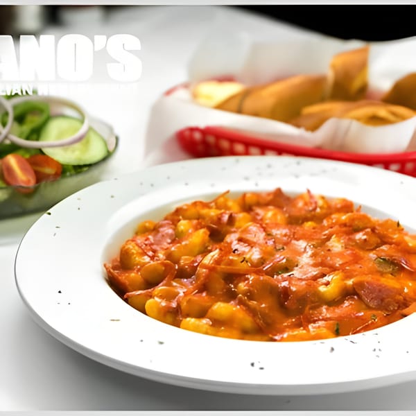 A white bowl of Romano's gnocchi in red sauce, with a side salad and bread rolls.