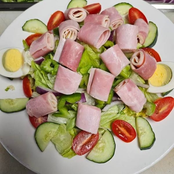 A vibrant Romano's Pizzeria salad with ham rolls, lettuce, tomatoes, cucumbers, and hard-boiled eggs.