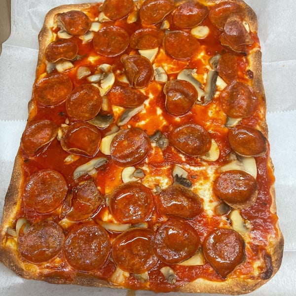 A rectangular Romano's Pizzeria pizza with pepperoni, mushrooms, and red sauce on a white surface.