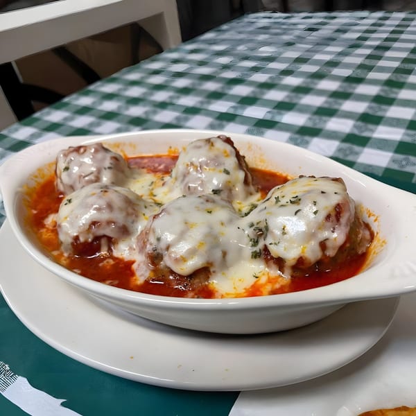 Baked meatballs covered in melted cheese and red sauce, served in a white dish on a green checkered tablecloth.