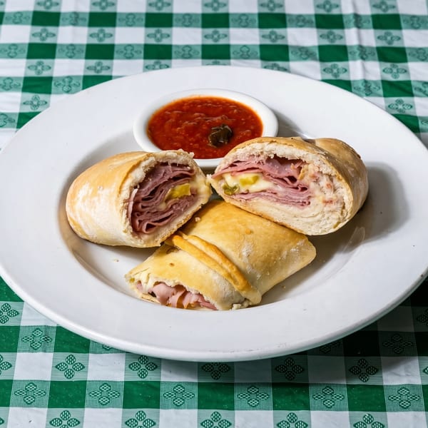 Three stromboli, two cut open to show ham and cheese, with a side of marinara sauce.