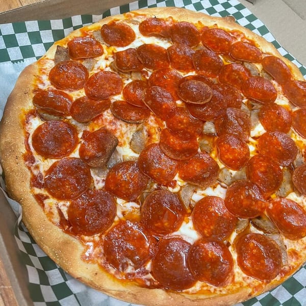 A Romano's Pizzeria pepperoni and sausage pizza with melted cheese on a checkered paper liner.
