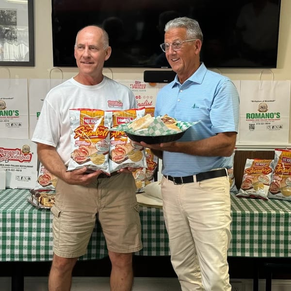 Two men holding Herr's "Stromboli" potato chip bags and a basket of stromboli sandwiches.
