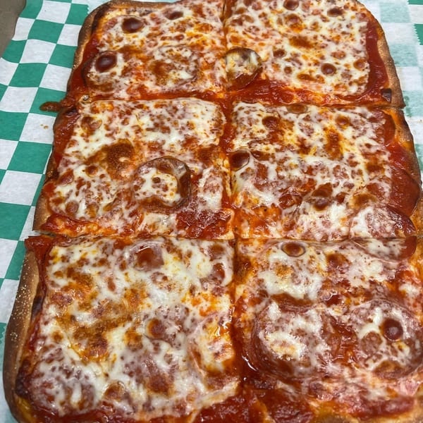 A rectangular Romano's Pizzeria pepperoni pizza, cut into six squares, on green and white checkered paper.