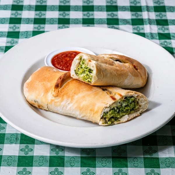 Two calzones filled with broccoli and cheese, served with a side of marinara sauce on a white plate.